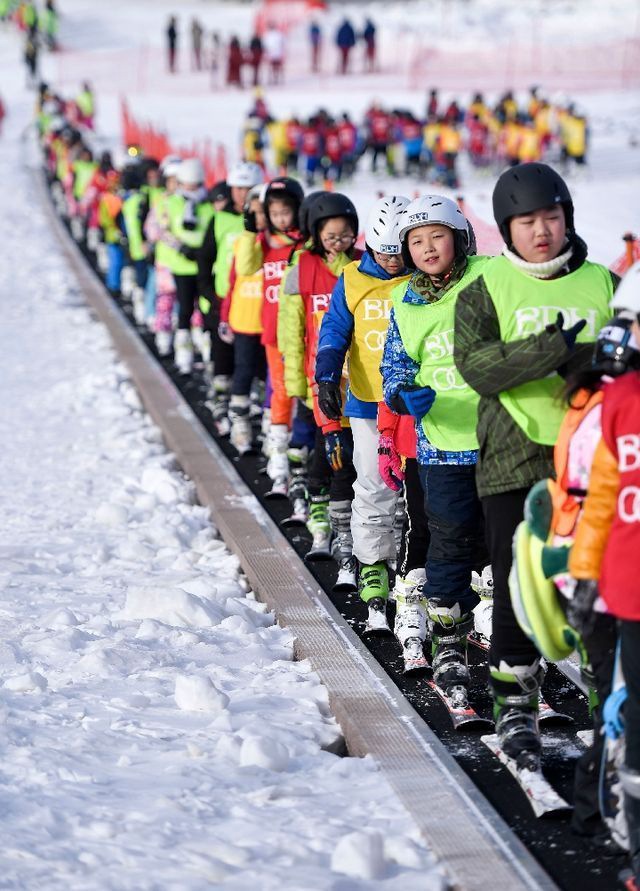 在吉林北大壶滑雪场，吉林市第二实验小学学生们在滑雪教练的带领下乘坐“魔毯”前往雪场学习区域。